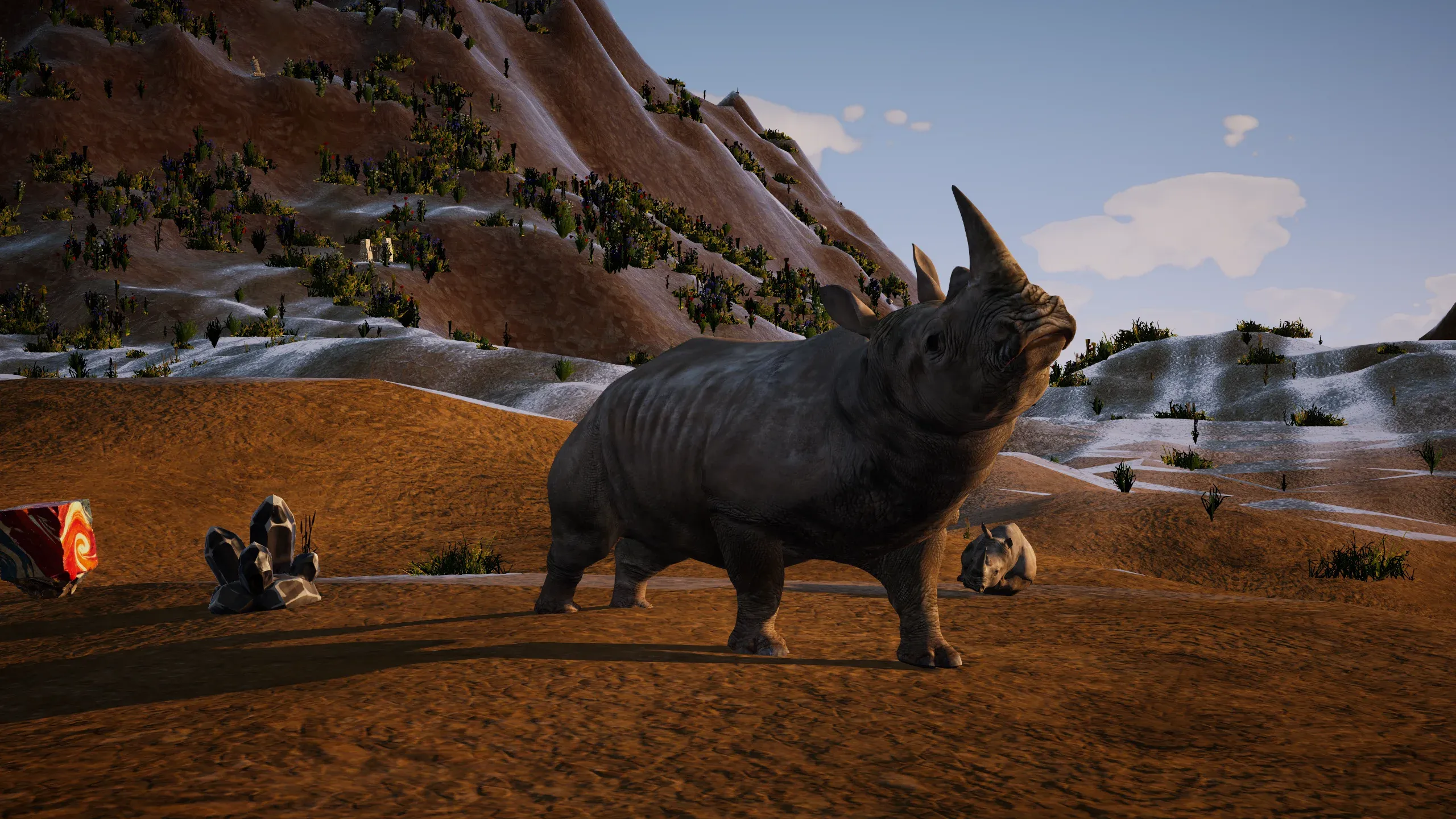 A rhinoceros in a dry valley below snowy slopes.